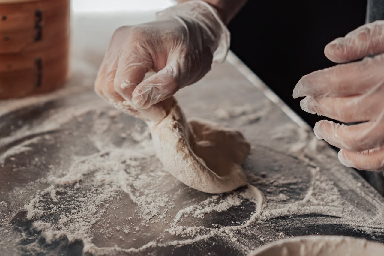 Hands kneading dough on a floured surface, detailed texture and motion captured in natural light.