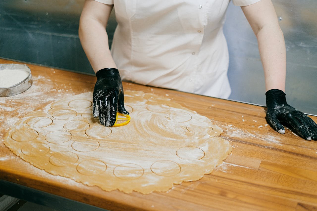 Chef using a cutter to prepare dough rounds for dumplings on a floured wooden table.